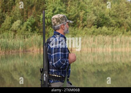 Uomo con fucile da caccia vicino al lago all'aperto Foto Stock