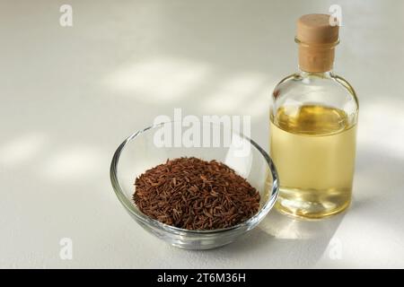 Semi di cumino persiano in ciotola e olio essenziale su tavola bianca Foto Stock