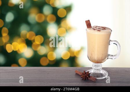 Delizioso eggnog in vetro su un tavolo di legno contro l'albero di Natale sfocato, spazio per il testo Foto Stock