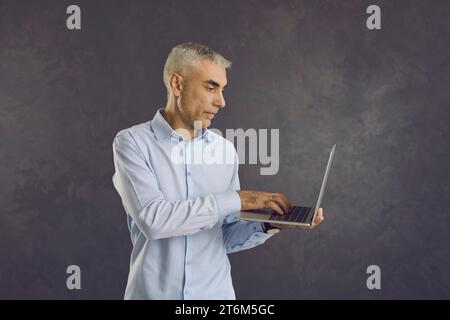 Foto in studio di un uomo anziano serio che tiene in braccio e usa il suo moderno computer portatile Foto Stock