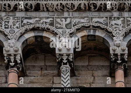 Scultura in marmo medievale e marmo intarsiato, aggiunto in stile romanico pisano nel 1200 alla parte inferiore del fronte ovest della Chiesa di San Michele in foro a Lucca, Toscana, Italia. I motivi marmorei intarsiati includono (da sinistra): cacciatore con uccello sul braccio, cane al fianco e tenendo una lancia; volpe che insegue cervi; uccello preda, ali spalmate, con la sua cattura; altri animali selvatici. Foto Stock