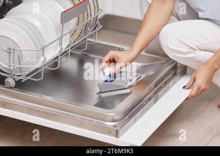 la mano femminile mette il tablet lavastoviglie in una lavastoviglie automatica con il piatto sporco all'interno della cucina Foto Stock