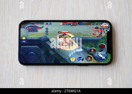 Honor of Kings gioco iOS per dispositivi mobili su schermo dello smartphone iPhone 15 su un tavolo di legno durante il gioco mobile. Giochi e intrattenimento mobili su dispositivi portatili Foto Stock