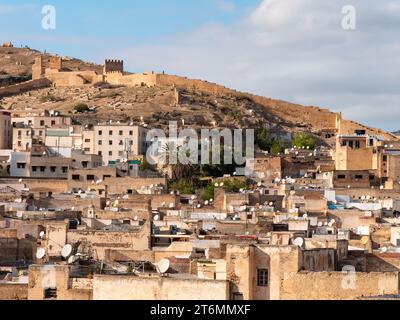 Dense neighborhood in Fes, Morocco, with the ruined Marinid tombs in the background on a bright afternoon Foto Stock