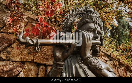 Statua in bronzo di Lord Krishna che suona sul flauto. Natura autunnale. Religione induista Foto Stock