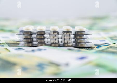 Vista frontale su pillole in vesciche su immagine offuscata di 100 euro bollette come sfondo, costo di farmaci per il grande pubblico. Foto di alta qualità Foto Stock