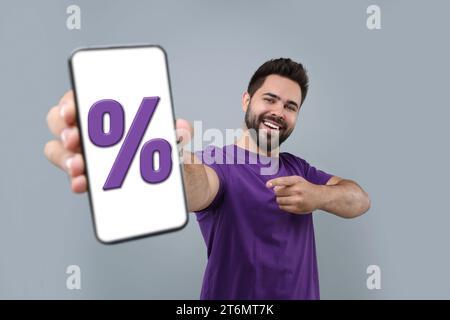 Sconto, offerta, vendita. Uomo che punta verso il telefono cellulare con la percentuale di accesso sullo schermo, sfondo grigio Foto Stock