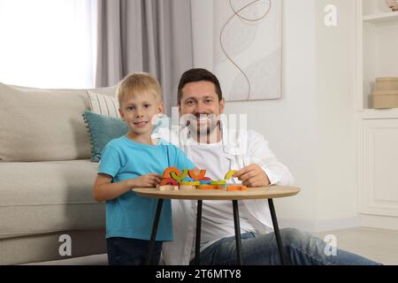 Sviluppo di competenze motorie. Padre felice che aiuta suo figlio a giocare con gli archi di legno colorati al tavolino in camera Foto Stock