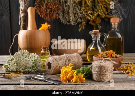 Erbe e fiori diversi, filo, forbici su tavolo di legno Foto Stock