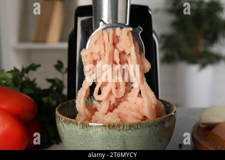 Tritatutto elettrico con tritatutto di pollo e prodotti sul tavolo al chiuso, primo piano Foto Stock