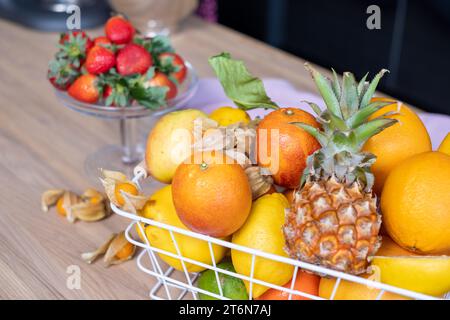 Succulenti frutti di sole in un cesto di metallo bianco, fragole rosse fresche in una ciotola di vetro, Physalis e un tovagliolo di lino su un tavolo di legno chiaro. Alta qualità Foto Stock