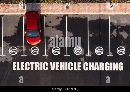 Vista aerea direttamente sopra una stazione di ricarica per veicoli elettrici con posti auto e segnaletica stradale che indica i vani di ricarica per auto elettriche Foto Stock