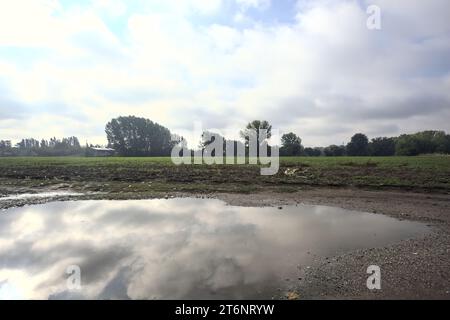 Immergiti in un sentiero vicino a un campo con il cielo gettato nell'acqua in una giornata nuvolosa nella campagna italiana Foto Stock