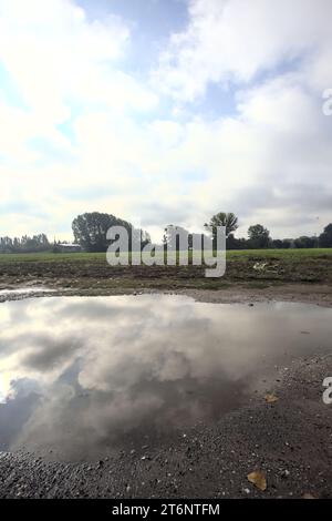 Immergiti in un sentiero vicino a un campo con il cielo gettato nell'acqua in una giornata nuvolosa nella campagna italiana Foto Stock