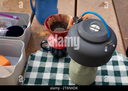 Bollitore con acqua calda riscaldata per versare o sgocciolare il caffè su un tavolo da picnic all'aperto Foto Stock