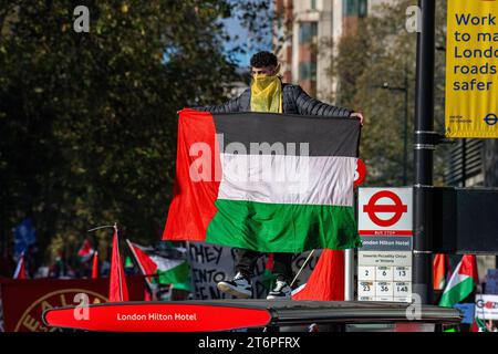 Londra, Regno Unito. 11 novembre 2023. Un uomo su una fermata dell'autobus con una bandiera palestinese grida mentre 300.000 sostenitori palestinesi marciano attraverso Londra Foto Stock