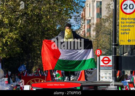 Londra, Regno Unito. 11 novembre 2023. Un uomo su una fermata dell'autobus con una bandiera palestinese grida mentre 300.000 sostenitori palestinesi marciano attraverso Londra Foto Stock