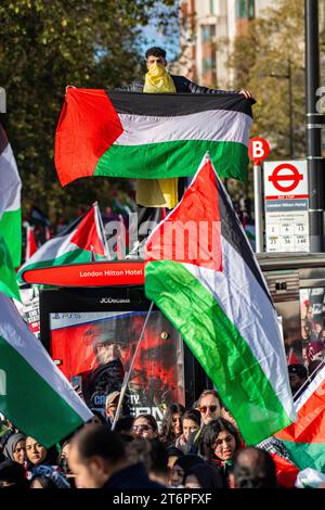 Londra, Regno Unito. 11 novembre 2023. Un uomo su una fermata dell'autobus con una bandiera palestinese grida mentre 300.000 sostenitori palestinesi marciano attraverso Londra Foto Stock