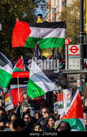 Londra, Regno Unito. 11 novembre 2023. Un uomo su una fermata dell'autobus con una bandiera palestinese grida mentre 300.000 sostenitori palestinesi marciano attraverso Londra Foto Stock