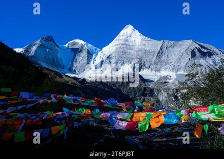 Un paesaggio di montagne innevate con colorate bandiere di preghiera buddiste che soffiano nel vento Foto Stock