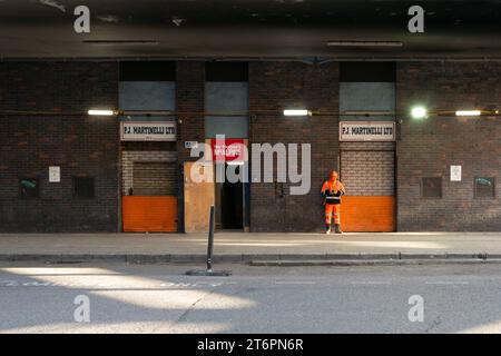 Un operaio edile si trova all'esterno di un edificio a Smithfield Market, Londra, accanto a un cartello per Sir Robert McAlpine, una società di costruzioni britannica Foto Stock