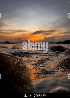 Un'immagine verticale di un incredibile tramonto che si riflette sulla superficie dell'oceano sulle rocce Foto Stock