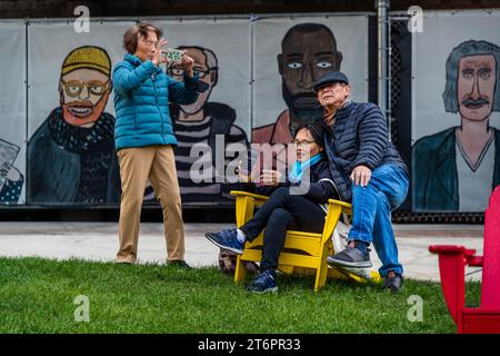 La Street art dell'artista di strada Dont Fret è stata esposta al 333 di West Walker Drive sul Chicago Riverwalk dal 2020. Mostra 55 ritratti di chicagoani "la gente nel tuo quartiere". Le persone si rilassano sulle sedie Adirondack poste sul prato del lungofiume di Chicago alla confluenza dei tre rami del fiume Chicago. Chicago, Illinois, Stati Uniti Foto Stock