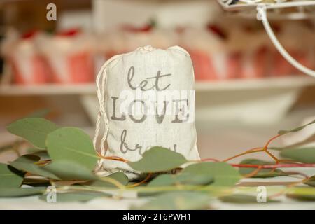 Borsa a tela con la scritta "Let Love Brew", un pezzo del centro per matrimoni, riempito di macine di cofee sul tavolo della cena Foto Stock