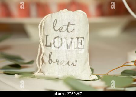 Borsa a tela con la scritta "Let Love Brew", un pezzo del centro per matrimoni, riempito di macine di cofee sul tavolo della cena Foto Stock