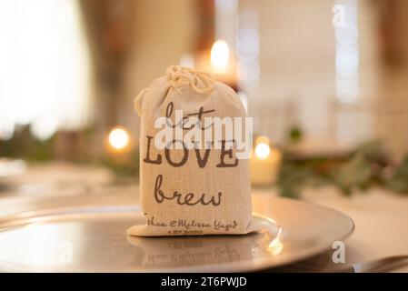 Borsa a tela con la scritta "Let Love Brew", un pezzo del centro per matrimoni, riempito di macine di cofee sul tavolo della cena Foto Stock