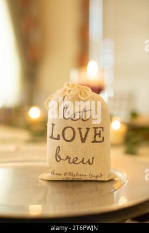 Borsa a tela con la scritta "Let Love Brew", un pezzo del centro per matrimoni, riempito di macine di cofee sul tavolo della cena Foto Stock