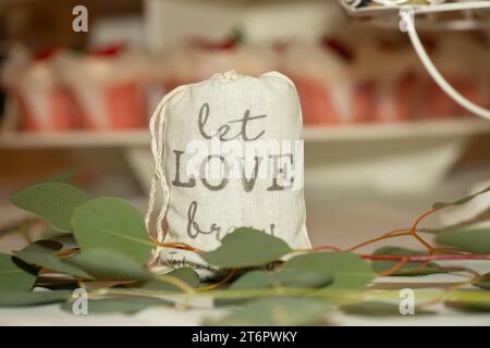 Borsa a tela con la scritta "Let Love Brew", un pezzo del centro per matrimoni, riempito di macine di cofee sul tavolo della cena Foto Stock