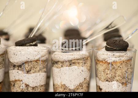 File di dolci al cioccolato e panna montata in piccole tazze di plastica con condimenti di biscotti al cioccolato al tavolo del dessert Foto Stock