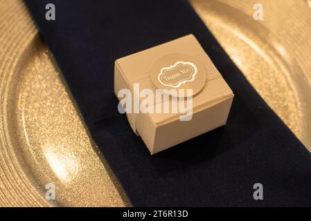 Scatola regalo in legno avvolta in pizzo e un'etichetta di ringraziamento sul tovagliolo nero su piatto dorato Foto Stock