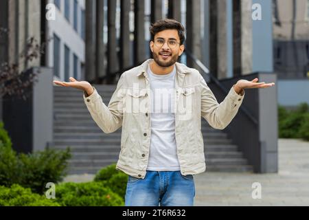 Cosa? Perché? Sorpreso l'uomo indiano frustrato che alza le mani chiedendo il motivo del fallimento, dimostrando incredulità irritazione da problemi all'aperto. Un uomo indù arabo confuso che si trova in una strada urbana Foto Stock