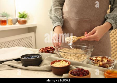 A fare la granola. Donna che mette fiocchi d'avena nella ciotola al tavolo in cucina, primo piano Foto Stock