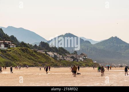 Verdi colline di alberi sempreverdi si innalzano sopra l'affollata Cannon Beach, Oregon, sotto un cielo estivo pallido. Foto Stock