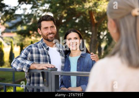 Rapporto amichevole con i vicini. Felice giovane coppia e donna anziana vicino a recinzione all'aperto Foto Stock