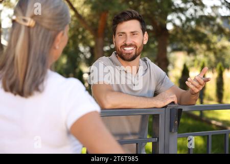 Rapporto amichevole con i vicini. Uomo felice e donna anziana vicino a recinzione all'aperto Foto Stock