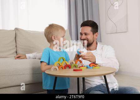 Sviluppo di competenze motorie. Padre felice che aiuta suo figlio a giocare con gli archi di legno colorati al tavolino in camera Foto Stock