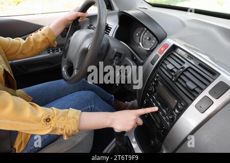 Scelta della radio preferita. Donna che preme il pulsante sull'audio del veicolo in auto, primo piano Foto Stock