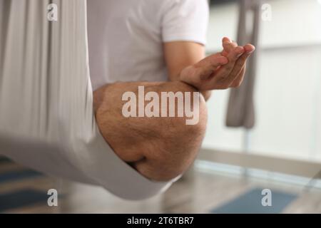 Uomo che medita in amaca da yoga con la mosca al chiuso, primo piano Foto Stock