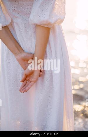 La donna sta vicino al mare scintillante con le mani dietro la schiena. Ritagliato. Senza volto. Vista posteriore Foto Stock