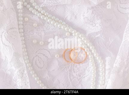 Due fedi nuziali dorati si trovano su una lussuosa parte vintage dell'abito da sposa della sposa con una serie di perle. Concetto di matrimonio. Vista dall'alto. Foto Stock