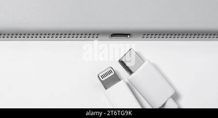 Cavo Apple Lightning a USB-C e gadget su un tavolo bianco con spazio vuoto, primo piano. Posto per la pubblicità. Concetto tecnologico. Foto Stock