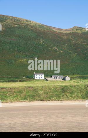 Una singola casa colonica bianca e degli edifici annessi si trovano di fronte a una collina con vista sulla spiaggia di Llangennith, nella penisola di Gower, nel Galles del Sud, Regno Unito Foto Stock