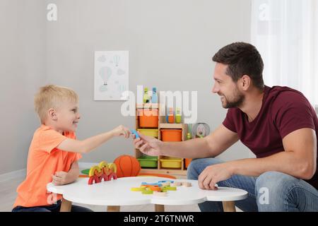 Sviluppo di competenze motorie. Padre felice che aiuta suo figlio a giocare con colorati archi di legno al tavolo bianco in camera Foto Stock