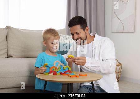 Sviluppo di competenze motorie. Padre felice che aiuta suo figlio a giocare con gli archi di legno colorati al tavolino in camera Foto Stock