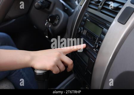 Scelta della radio preferita. Donna che preme il pulsante sull'audio del veicolo in auto, primo piano Foto Stock