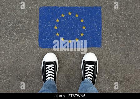Immigrazione. Uomo in piedi sull'asfalto vicino alla bandiera dell'Unione europea, vista dall'alto Foto Stock